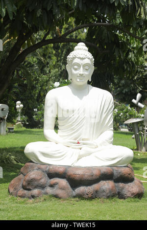 Bangalore, Karnataka India-June 04 2019: weißer Buddha Statue, die in der Meditation Körperhaltung auf Tisch aus Stein mit der Natur als Hintergrund. Stockfoto