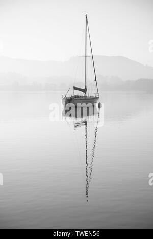 Schöne unplugged Landschaft Bild der Segelyacht sitzt immer noch in ruhigen See Wasser im Lake District während der friedlichen nebligen Herbst Sonnenaufgang Stockfoto