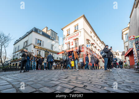 Paris, Frankreich, 12. April 2019: Leute auf der Terrasse des Restaurant Le Consulat in Montmartre am Abend sitzen an einem sonnigen Tag mit Kopfsteinpflaster im Vordergrund. Stockfoto