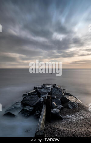 Rock buhnen oder Meer Abwehr rechts von Southwold Pier wie die Sonne kommt. Stockfoto