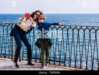 Mutter und Sohn im Water's Edge unter selfie mit Smartphone und lächelnd in die Insel Ortygia in Syrakus auf Sizilien. Stockfoto