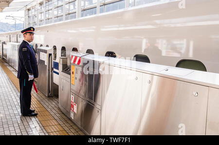 Dirigent in Uniform stehend auf Bahnsteig holding Flag neben Shinkansen in Himeji Station in Japan. Stockfoto