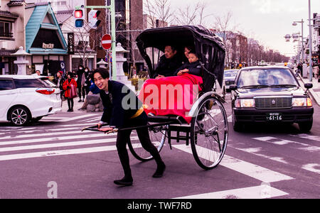 Familie Rikscha-fahrt in belebten Straße mit der rikscha Fahrer Kamera suchen und lächelnd in Kamakura, Japan. Stockfoto