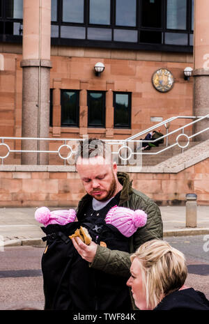 Paar im Freien mit Mann, zwei junge Babys im Körper Schlinge essen Sandwich in der Quayside entfernt von Newcastle upon Tyne in England. Stockfoto