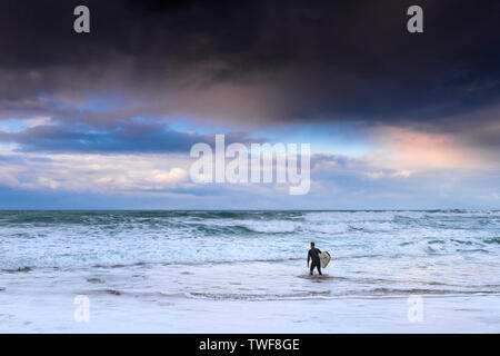 Schöne pastell Farben in den Himmel, wie die Sonne über eine einsame Surfer gehen in das Meer bei Fistral Beach in Newquay in Cornwall. Stockfoto