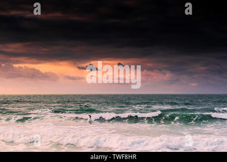 Einen spektakulären Sonnenuntergang als einsame Surfer reitet eine Welle an Fistral Beach in Newquay in Cornwall. Stockfoto