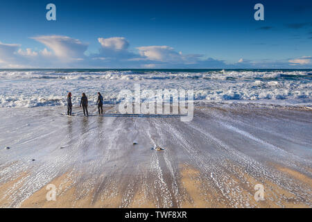 Menschen in Neoprenanzüge stehen an der Küste bei Fistral Beach in Newquay in Cornwall. Stockfoto