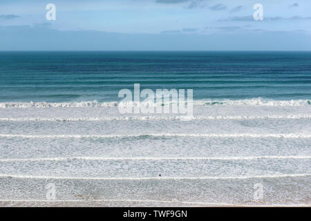 Die kleine Figur eines Surfer aus zu Fuß in die ankommenden Wellen bei Watergate Bay in Cornwall. Stockfoto