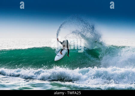Ein Surfer, ein Surfbrett auf dem Kamm eines Jade farbige Welle Fistral in Newquay in Cornwall. Stockfoto