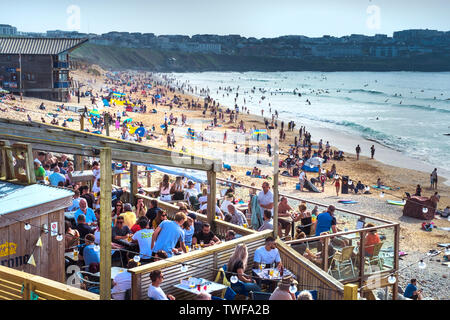 Urlauber genießen die Sonne auf einer belebten Fistral Beach in Newquay in Cornwall. Stockfoto