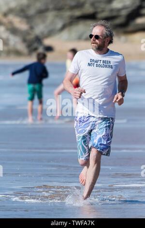 Ein reifer Mann, der ein T-Shirt mit einem lustigen Slogan Joggen entlang der Küste auf den Fistral Beach in Newquay in Cornwall. Stockfoto