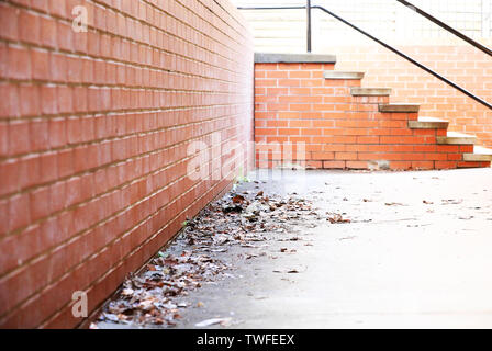 Street Scene von einer Ecke einen Pfad mit trockenen Blätter im Herbst. Tiefe Perspektive mit roten Ziegeln und Beton. Schritte Treppenhaus zurück. Urban Konzept. Stockfoto