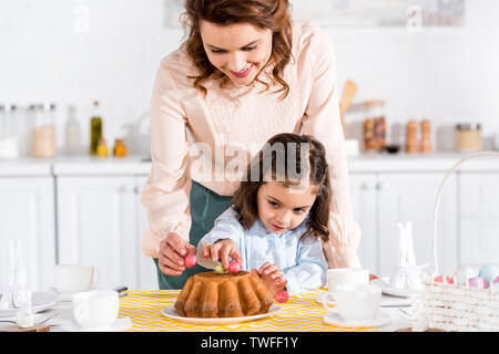 Lächelnde Mutter und Tochter Dekoration Ostern Kuchen mit Eier in der Küche Stockfoto