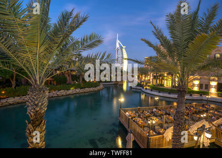 Die schöne Uferpromenade von Souk Madinat Jumeirah und das 7-Sterne Hotel Burj al Arab zeichnen sich durch eine elegante Palmen in Dubai eingerahmt.