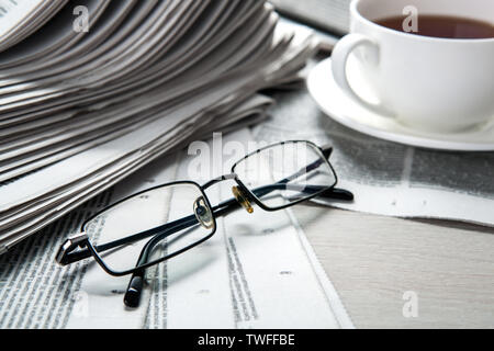 Gläser auf Zeitungen und einer Tasse Kaffee auf dem Tisch closeup Stockfoto