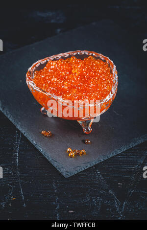 Lachs roter Kaviar in Schale mit Löffel auf schwarzem Hintergrund. Exquisite Delikatesse Stockfoto