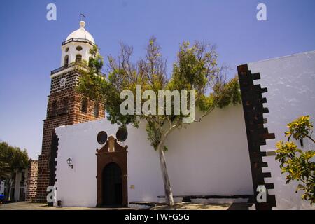 TEGUISE, LANZAROTE - juin 2013 3. 2019: Blick auf der Wand des weißen alte Kirche mit Bäumen gegen den blauen Himmel Stockfoto