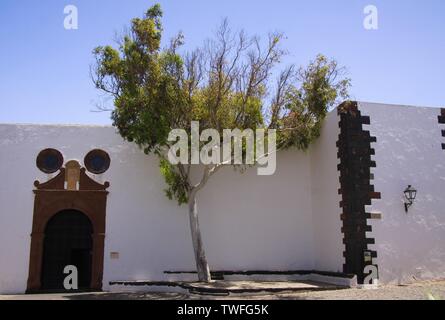 TEGUISE, LANZAROTE - juin 2013 3. 2019: Blick auf der Wand des weißen alte Kirche mit Bäumen gegen den blauen Himmel Stockfoto