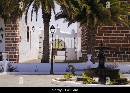 TEGUISE, LANZAROTE - juin 2013 3. 2019: Blick über Platz mit Palmen auf alten weißen Kirche gegen den blauen Himmel Stockfoto