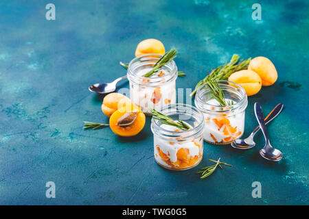 Naturjoghurt mit Stücken von Aprikosen-, Walnuss- und Rosmarin in kleinen Gläsern auf lblue Hintergrund. Stockfoto