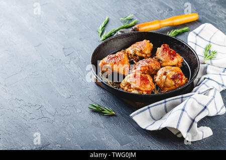 Hühnerkeule gebraten mit Rosmarin in einer gusseisernen Pfanne und Rosmarin auf Hintergrund Stockfoto