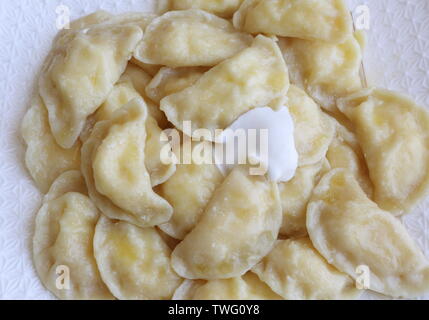 Teigtaschen mit Quark, saure Sahne auf einem weißen Teller auf braunem Hintergrund Stockfoto