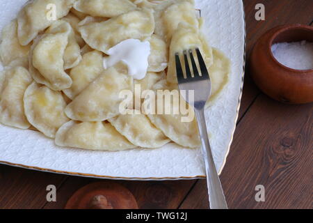 Teigtaschen mit Quark, saure Sahne auf einem weißen Teller auf braunem Hintergrund Stockfoto