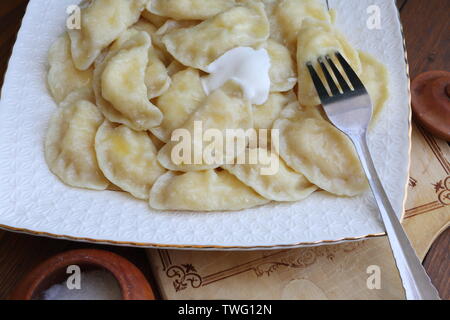 Teigtaschen mit Quark, saure Sahne auf einem weißen Teller auf braunem Hintergrund Stockfoto