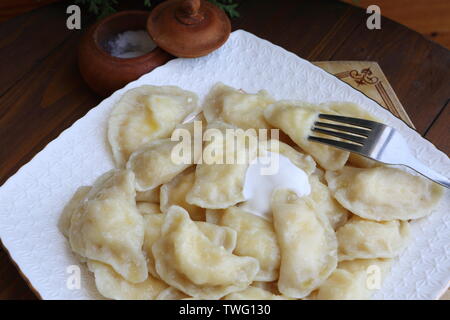 Teigtaschen mit Quark, saure Sahne auf einem weißen Teller auf braunem Hintergrund Stockfoto