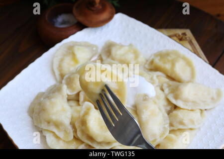 Teigtaschen mit Quark, saure Sahne auf einem weißen Teller auf braunem Hintergrund Stockfoto