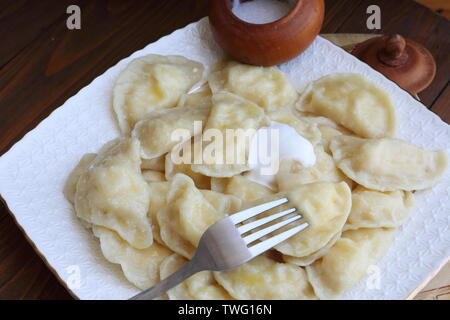 Teigtaschen mit Quark, saure Sahne auf einem weißen Teller auf braunem Hintergrund Stockfoto