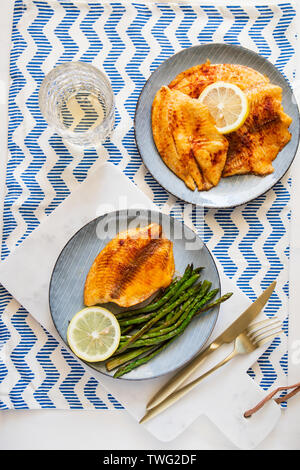 Gebackene Tilapia-fisch mit Spargel auf einer Keramikplatte. Gesunde mediterrane Diät Mittag- oder Abendessen. Stockfoto