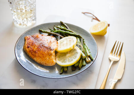 Gebackene Tilapia-fisch mit Spargel auf einer Keramikplatte. Gesunde mediterrane Diät Mittag- oder Abendessen. Stockfoto