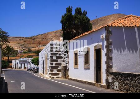 BETANCURIA, Fuerteventura - JUIN 14. 2019: Blick entlang der Straße mit traditionellen weißen Häusern auf trockenen Hügel unter blauen Himmel Stockfoto