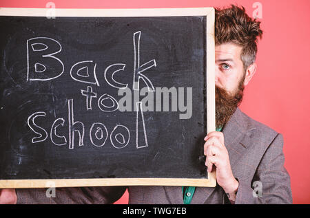 Sind Sie bereit, zu studieren. Lehrer oder Schulleiter begrüßt zurück zur Schule. Lehrer versteckt sich hinter Tafel. Vorbereitung Anfang Schuljahr. Lehrer peeking aus der Tafel über den roten Hintergrund. Stockfoto