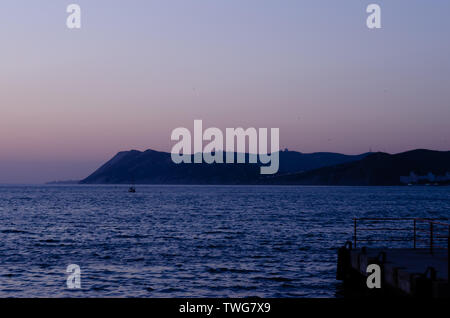 Dramatische unscharfer Sonnenuntergang Landschaft Hintergrund. Schöne flammenden Sonnenuntergang über leuchtend blaue Meer, Pier, Jet Trails, orange Himmel über es mit tollen golden Stockfoto