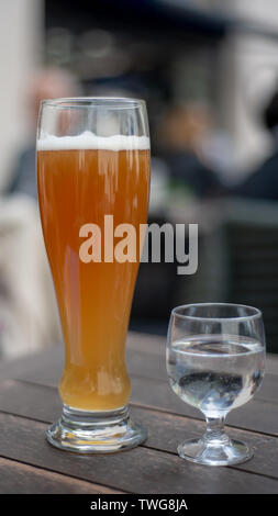 Weißbier auf dem Tisch voller Bier mit halb vollen Glas Mineralwasser auf hölzernen Tisch draußen serviert, von der Seite gesehen Stockfoto