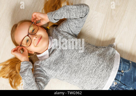 Blick von oben auf ein kleines Mädchen mit Brille auf dem Boden liegend Stockfoto