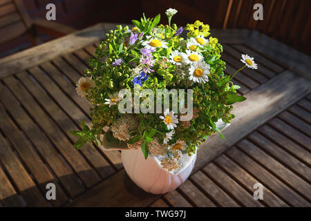 Blumenstrauß aus wilden Blumen in Weiß Vase auf Holztisch. Stockfoto