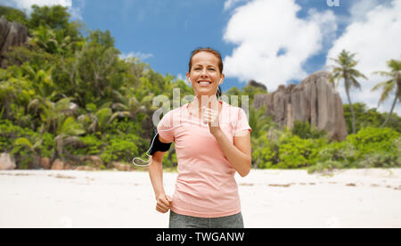 Frau mit Kopfhörer und Armband laufen am Strand Stockfoto