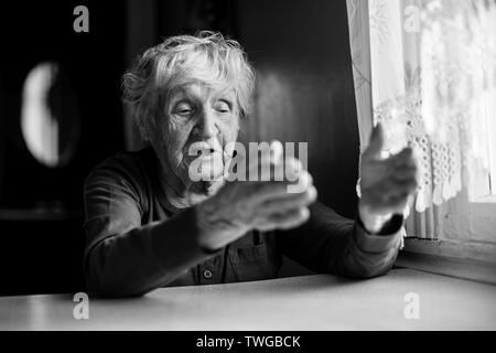 Die alte Dame sitzt Reden gestikulierend am Küchentisch. Schwarz-weiß Foto. Stockfoto