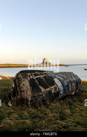 Ein altes Fischerboot wurde umgedreht und diente als Bootshütte am Strand der Heiligen Insel Lindisfarne mit Schloss Lindisfarne in der Stockfoto