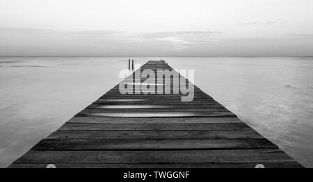 Dämmerung auf einem Holzsteg Stretching in den stillen Ozean in beeindruckenden Schwarz und Weiß Stockfoto