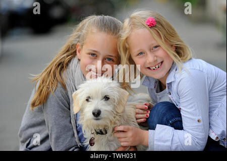 Zwei Schwestern mit ihren kreuzen Hund auf einem Bürgersteig in Düsseldorf, Deutschland. Stockfoto