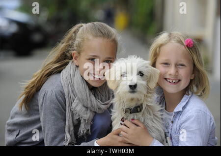 Zwei Schwestern mit ihren kreuzen Hund auf einem Bürgersteig in Düsseldorf, Deutschland. Stockfoto