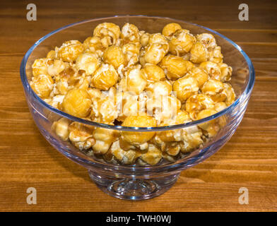 Toffee popcorn beschichtet Snack, angehäuft in eine Glasschüssel auf einer Kiefer Tisch. Stockfoto