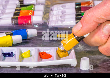 Des Menschen Hand zusammendrücken Aquarellfarbe aus einem Rohr in ein Fach mit Fächern für separate Farben. Mehrere Rohre der Farben sind in der Nähe. Stockfoto