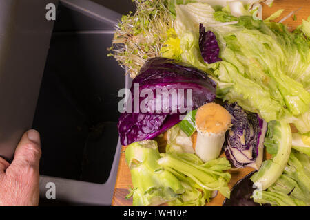 Stücke von Rohstoffen pflanzlicher Nahrung Abfälle bereit, von einer Küche Oberfläche in eine offene Swing bin geschoben werden. Stockfoto