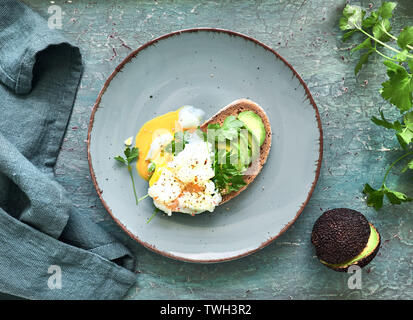 Avocado Sandwich mit dunkles Brot, geschnitten Avocado und pochiertem Ei, flach auf dunklen rustikalen Hintergrund Stockfoto