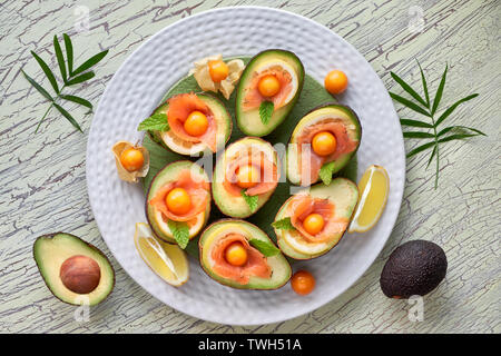 Avocado Boote mit geräuchertem Lachs, Zitrone, Physalis und Minzeblatt, Ansicht von oben an der strukturierten Hintergrund Stockfoto